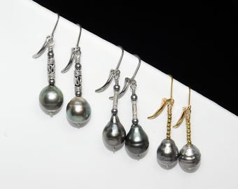 May include: Several pairs of dangle earrings with dark gray, round pearls. The earrings have silver and gold-colored metal hooks and decorative elements. The pearls are approximately 0.5 inches in diameter.