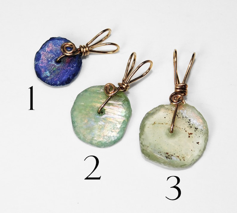 Puede incluir: Tres colgantes hechos a mano con dise&ntilde;os envueltos en alambre. Un colgante es de color azul oscuro, mientras que los otros dos son de color verde claro. Cada colgante tiene una forma irregular &uacute;nica, y el alambre es dorado.