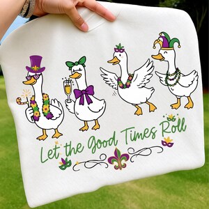 Könnte beinhalten: Weißes Sweatshirt mit einem Design von vier Cartoon-Gänsen in festlicher Kleidung. Die Gänse tragen Hüte, Fliegen und Perlen. Der Schriftzug "Let the Good Times Roll" steht in grüner Schrift unter den Gänsen.