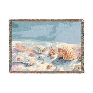 May include: A rectangular woven throw blanket featuring a beach scene with various seashells scattered across a sandy shore. The design includes shades of light blue, beige, and white, finished with a decorative fringed edge on all four sides.