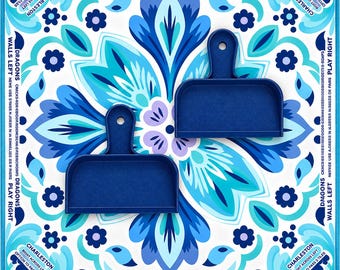 Könnte beinhalten: Zwei dunkelblaue Kunststoffschieber für ein Fliesenspiel liegen auf einer quadratischen Matte mit einem symmetrischen Blumenmuster in Blau, Hellblau und Weiß. Die Matte enthält aufgedruckte Spielanleitungen, wie etwa die Regeln für Charleston und Dragons.