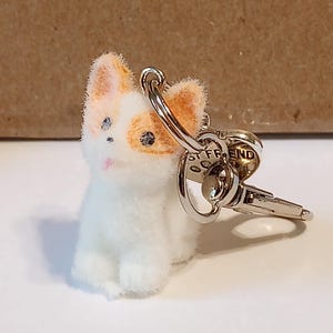 Op de afbeelding: Een witte en oranje pluche katten sleutelhanger met een zilveren sleutelring en sleutel. De sleutelhanger heeft een kleine roze neus en blauwe ogen. Op de sleutelring staat "BEST FRIEND".