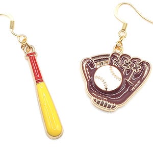 May include: Gold-tone baseball earrings. One earring features a yellow and red baseball bat, the other a brown baseball glove with a white baseball. The earrings have gold-coloured fish hook closures.