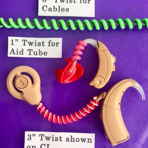 Puede incluir: La imagen muestra aud&iacute;fonos y accesorios relacionados. En la parte superior, un cable en espiral verde, etiquetado como "5" Twist for Cables". Debajo, una espiral roja y blanca conectada a un aud&iacute;fono, etiquetada como "3" Twist shown on CI". Otro accesorio est&aacute; etiquetado como "1" Twist for Aid Tube".