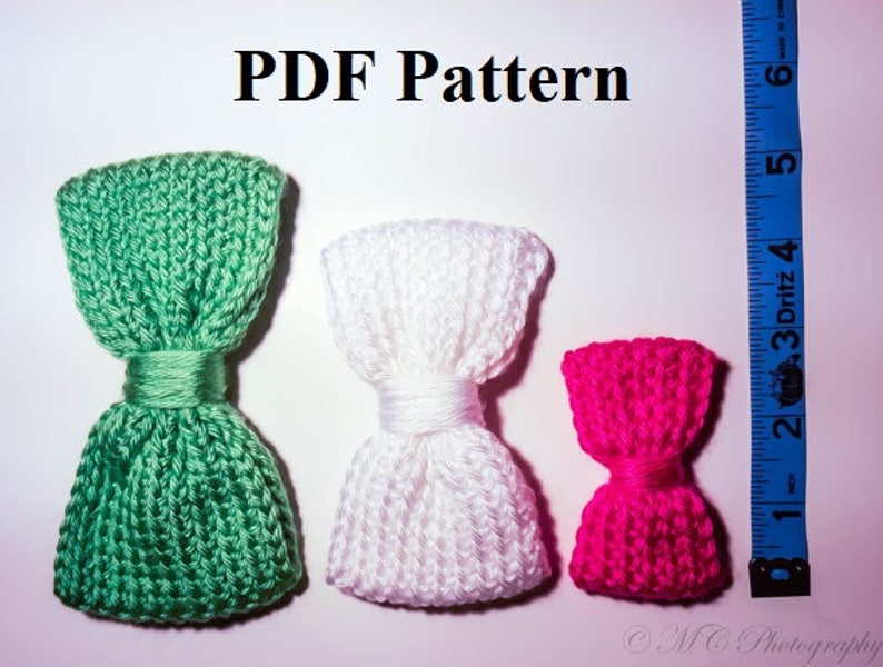 May include: Three knitted bow ties in different colors: green, white, and pink. The bow ties are arranged in a row from left to right, with the green bow tie on the left, the white bow tie in the middle, and the pink bow tie on the right. The bow ties are all made with a similar knit stitch pattern.