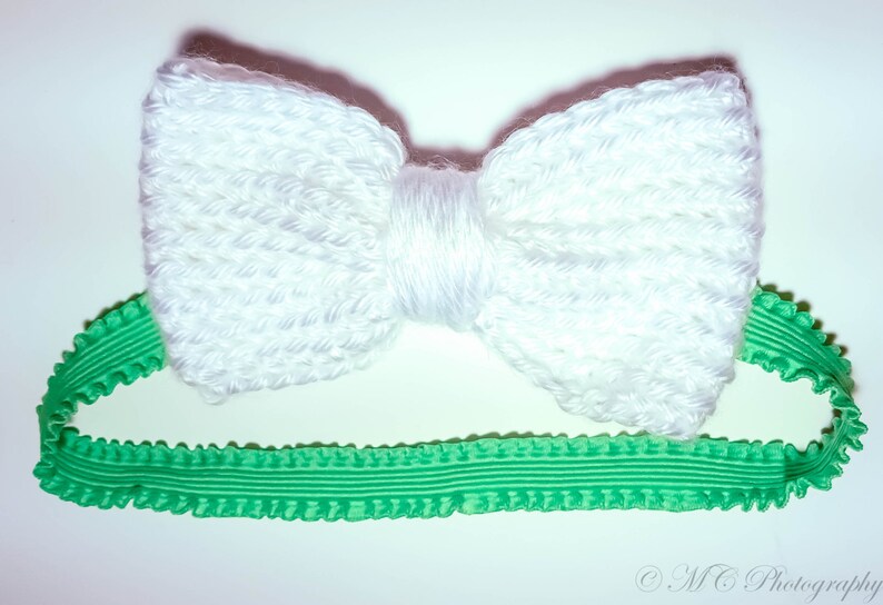 May include: A white crocheted bow headband with a green ruffled elastic band.