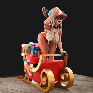 May include: A figurine of a deer-like character in a Santa hat and bikini, standing on a red sleigh filled with wrapped gifts. The sleigh has gold accents and is decorated with colorful lights. The background is dark.