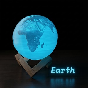 May include: A blue illuminated Earth globe lamp, showcasing detailed geographical features. The globe is supported by a wooden stand. The word "Earth" glows in blue beneath it. The lamp provides a soft, ambient light, suitable for a bedside table or desk.