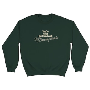 May include: Dark green sweatshirt with the text "You're what the French call Les Incompétents" in a cream-colored font. The sweatshirt has long sleeves and a crew neck.