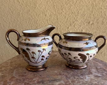 Juego de cremera y azucarero de cobre antiguo con acabado brillante, loza inglesa con brillo iridiscente, esmalte rosa nacarado, motivo floral pintado a mano.