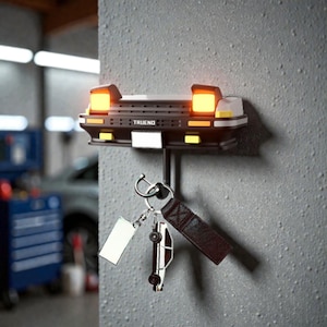 Puede incluir: Un llavero con forma de coche en blanco y negro con la palabra "TRUEND" en la parte delantera. El llavero tiene dos luces naranjas y una matrícula blanca. Debajo cuelgan llaves con un dije de coche y una correa de cuero.