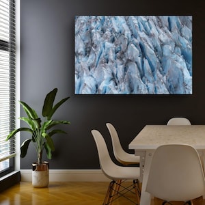 Op de afbeelding: Een groot, rechthoekig canvasdoek met een close-up van een gletsjer. Het kunstwerk toont de ijzige blauwe en grijze tinten van het gletsjeroppervlak, met diepe spleten en gedetailleerde texturen. De print wordt weergegeven op een donkergrijze muur.