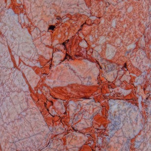 Puede incluir: Primer plano de una superficie de piedra natural con un patrón llamativo. La piedra presenta una mezcla de tonos rojos, blancos y grises, con vetas prominentes y texturas fracturadas. El efecto general es un diseño visualmente rico y complejo, adecuado para aplicaciones decorativas.