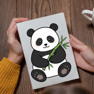 May include: A gray card featuring a cartoon panda bear holding bamboo. The panda is black and white with pink cheeks and black eyes. The bamboo is green. The card is held by a person wearing a yellow sweater.