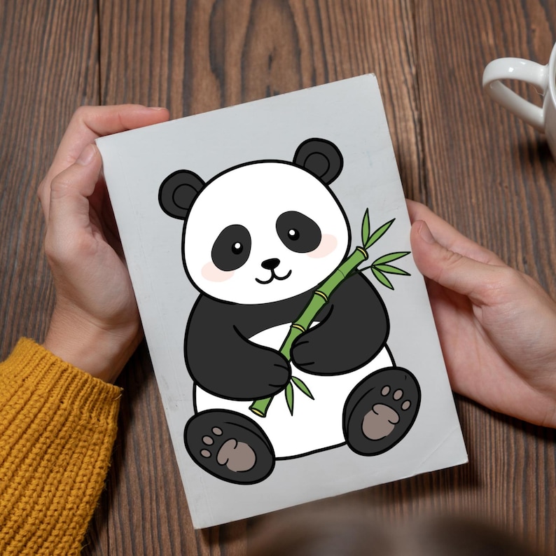 May include: A gray card featuring a cartoon panda bear holding bamboo. The panda is black and white with pink cheeks and black eyes. The bamboo is green. The card is held by a person wearing a yellow sweater.