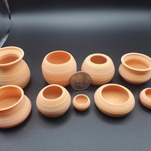 May include: A collection of small, terracotta-colored pottery vessels of varying sizes. The vessels have a striped pattern and a smooth finish. The collection includes pots with and without rims, and a coin is placed among them for scale.