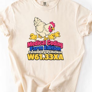 May include: A cream-coloured t-shirt featuring a graphic of a white hen with three yellow chicks. The text reads: Medical Coding Farm Edition Pecked by a Chicken W61.33XA. The design uses pink, blue, and yellow lettering with a distressed texture.