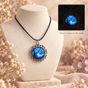 May include: A round pendant necklace featuring a reproduction of The Starry Night painting in a silver-toned ornate filigree frame on a black cord. An inset shows the pendant glowing in the dark with the text Make it glow in the dark.