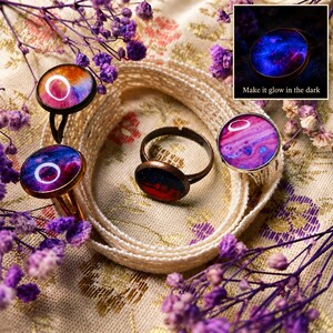 May include: Four rings with circular settings featuring colorful abstract patterns in shades of pink, purple, blue, and orange. One ring displays a dark, glowing nebula design with the text Make it glow in the dark visible in a small inset.