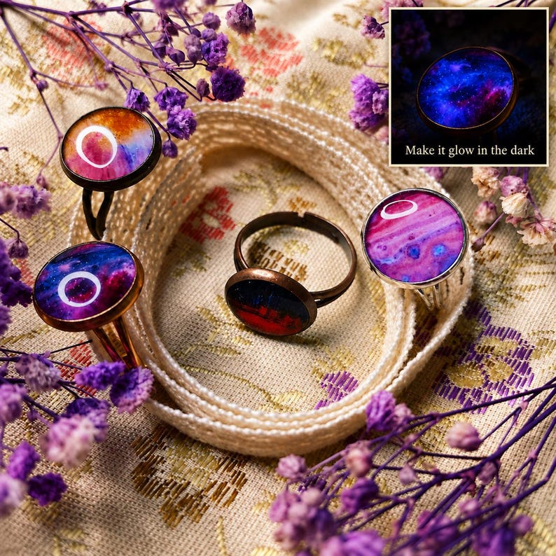 May include: Four rings with circular settings featuring colorful abstract patterns in shades of pink, purple, blue, and orange. One ring displays a dark, glowing nebula design with the text Make it glow in the dark visible in a small inset.