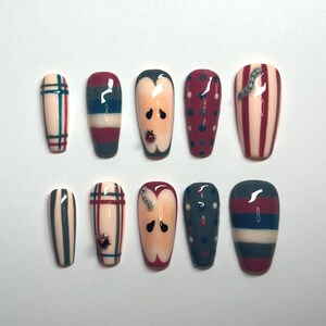 May include: A set of ten press-on nails featuring various designs including plaid patterns, horizontal stripes, vertical stripes, polka dots, and apple slice motifs with small three-dimensional ladybug and worm embellishments in red, blue, and cream.