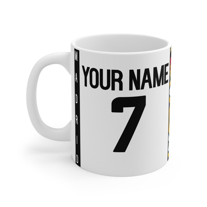 Peut inclure: Mug en c&eacute;ramique blanche avec un design de maillot. Le mug pr&eacute;sente le texte "YOUR NAME" au-dessus du num&eacute;ro "7" en noir. Le mot "MADRID" est imprim&eacute; verticalement sur le c&ocirc;t&eacute;. Un mug sur le th&egrave;me du sport.