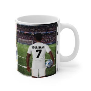 Peut inclure: Mug en c&eacute;ramique blanche avec un joueur de football en uniforme blanc, portant le num&eacute;ro 7 et le texte "YOUR NAME". Le fond repr&eacute;sente un terrain de football et un stade, avec le mot "MADRID" imprim&eacute; sur le c&ocirc;t&eacute;.