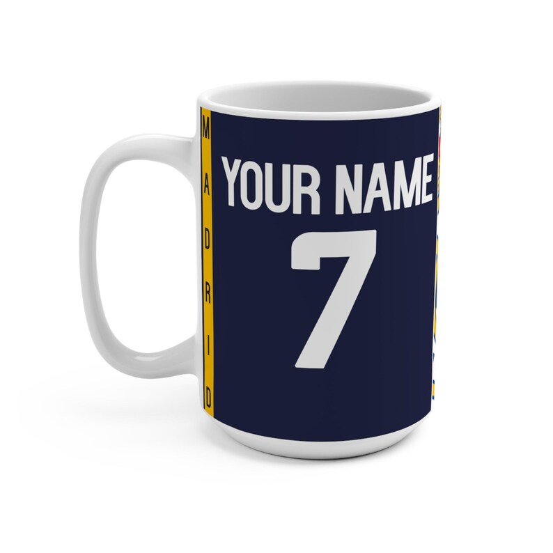 Peut inclure: Mug en c&eacute;ramique blanche avec un motif bleu marine. Le mug pr&eacute;sente le texte "YOUR NAME" au-dessus du chiffre "7" en blanc. Le mot "MADRID" est imprim&eacute; verticalement sur le c&ocirc;t&eacute; en jaune et blanc.