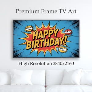 May include: A framed comic book style art print with the words "HAPPY BIRTHDAY!" in yellow and red against a blue background. The print includes "WOW," "ZAP," and "BOOM" sound effects. The art is displayed above a white couch.