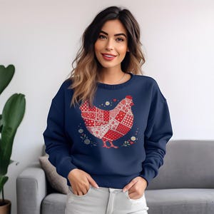 Może przedstawiać: Granatowa bluza z nadrukiem patchworkowego kurczaka w kolorze czerwonym i białym. Kurczak otoczony jest małymi białymi kwiatami i sercami. Bluza ma okrągły dekolt.