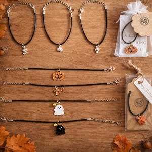 Può includere: Una collezione di braccialetti in cordino nero con vari ciondoli in metallo, tra cui una zucca, uno scoiattolo, un fantasma e una foglia. Alcuni braccialetti hanno catenelle e chiusure a moschettone color argento. Due sono in bustine trasparenti.