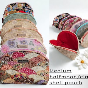 May include: A collection of medium halfmoon/clam shell pouches in various floral and patterned fabrics. The pouches have a zipper closure and a "handmade" tag. One pouch is open, revealing a red interior. White daisy flowers are in the foreground.