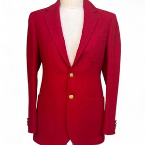 Puede incluir: Un blazer de color rojo vibrante con solapa de muesca, dos botones dorados en el cierre central delantero, un bolsillo de parche en el pecho y dos bolsillos de parche inferiores. Las mangas tienen pequeños botones dorados en los puños.