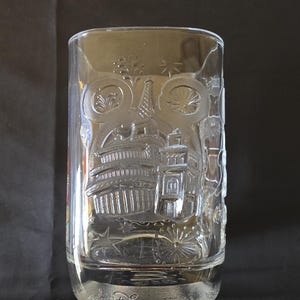 May include: Clear glass tumbler with etched Disney World imagery. The design includes iconic landmarks and fireworks. The base of the glass is inscribed with "Disney World".