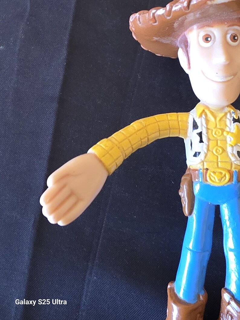 May include: A Woody action figure, featuring a brown cowboy hat, yellow shirt with black and white accents, blue jeans, and brown boots. The figure has a sheriff's badge and a holster. The figure is a popular character from the Toy Story franchise.