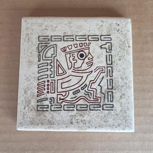 May include: Square ceramic tile with a beige background and a brown geometric design. The design features a stylized figure with a crown, surrounded by a rectangular border. The tile has a slightly textured surface.