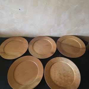May include: Five wooden charger plates with a warm, natural wood grain finish. Each plate has a wide, flat rim and a slightly recessed centre. The plates are arranged in a semi-circular pattern, showcasing their simple, elegant design.