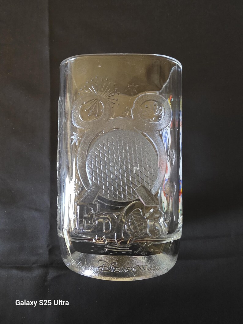 May include: Clear glass tumbler with embossed design featuring a Mickey Mouse head, a tennis ball, and the text "EPCOT" and "Disney World". The glass has a rectangular shape and is suitable for cold beverages.