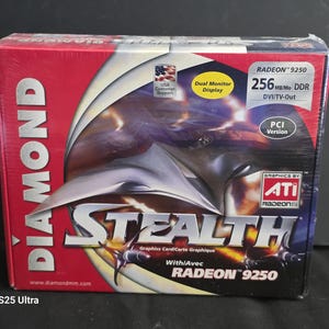 May include: A Diamond Stealth graphics card box featuring a red and black design with a central abstract metallic graphic. The packaging displays the text Radeon 9250, 256MB DDR, DVI/TV-Out, PCI Version, and ATI Radeon graphics branding.