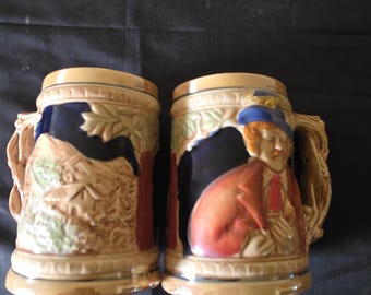 2 vintage keramische bierpullen uit de jaren 60 in Duitse stijl met een man met een pijp aan de ene kant en een dorp met huisjes en bergen aan de andere kant