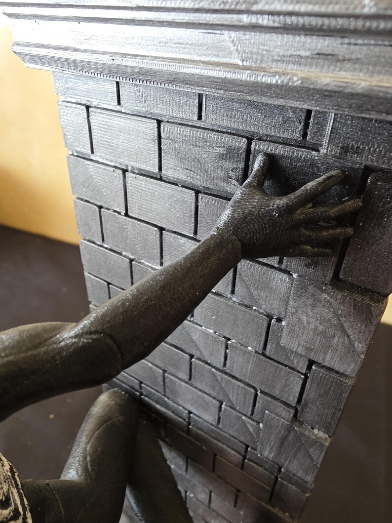 K&ouml;nnte beinhalten: Eine dunkelgraue Backsteinmauer mit dekorativer Oberseite. Ein dunkelgrauer Arm und eine Hand greifen nach der Mauer. Die Ziegel haben ein strukturiertes Aussehen.
