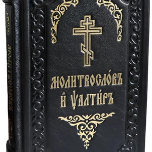 May include: Black book with gold lettering and a cross design. The cover features ornate gold accents and text. The spine also has gold lettering. The book appears to be a religious text.