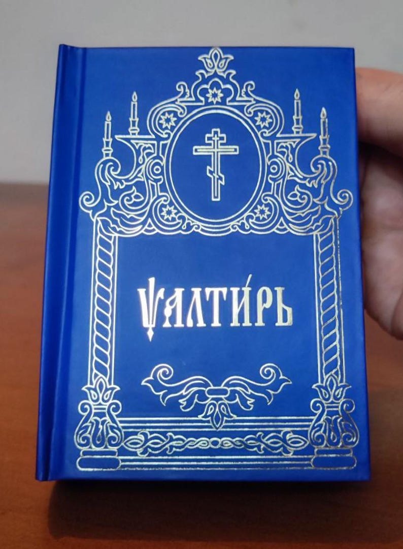 May include: A blue book with gold decorative accents and text. The cover features a cross within a circle, surrounded by ornate designs. The book's title is written in gold lettering.