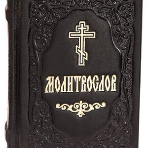May include: A black book with gold lettering and a gold cross. The cover has an ornate embossed design. The text "MOLITVOSLOV" is displayed in gold lettering. The book is closed and appears to be new.