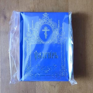 May include: A white ceramic mug with a black handle and the text "But First, Coffee" in a bold, black font. The mug is set against a blurred background, suggesting a cozy setting.