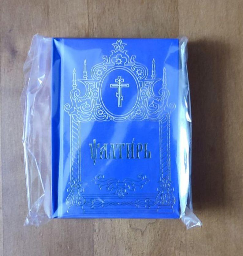 May include: A white ceramic mug with a black handle and the text "But First, Coffee" in a bold, black font. The mug is set against a blurred background, suggesting a cozy setting.