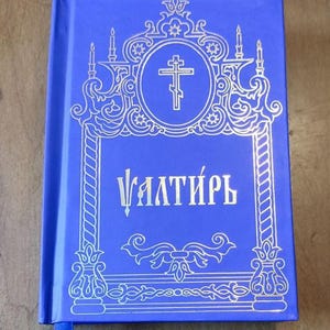 May include: A blue book with gold ornate detailing and the Cyrillic word "Ѱалти́рь" on the cover. The cover features a cross within a circle, surrounded by decorative elements. A blue ribbon bookmark is visible.