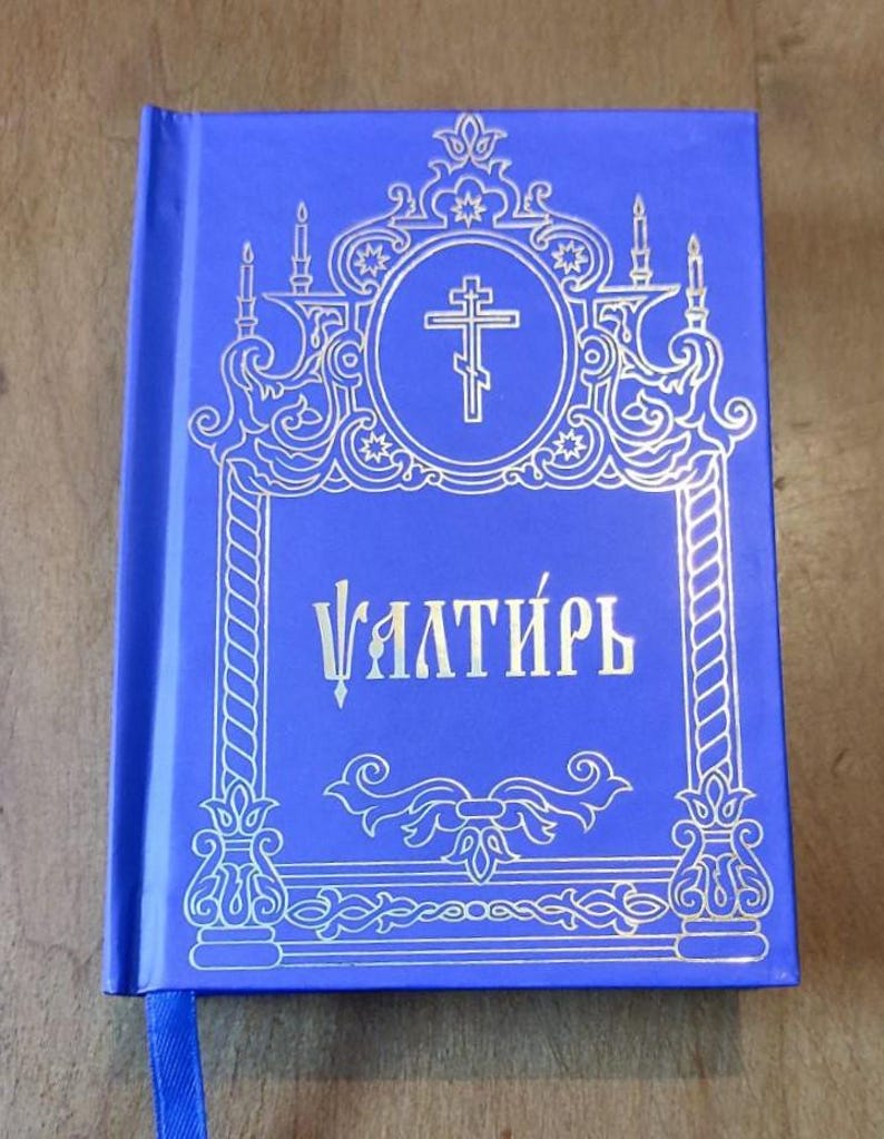 May include: A blue book with gold ornate detailing and the Cyrillic word "Ѱалти́рь" on the cover. The cover features a cross within a circle, surrounded by decorative elements. A blue ribbon bookmark is visible.