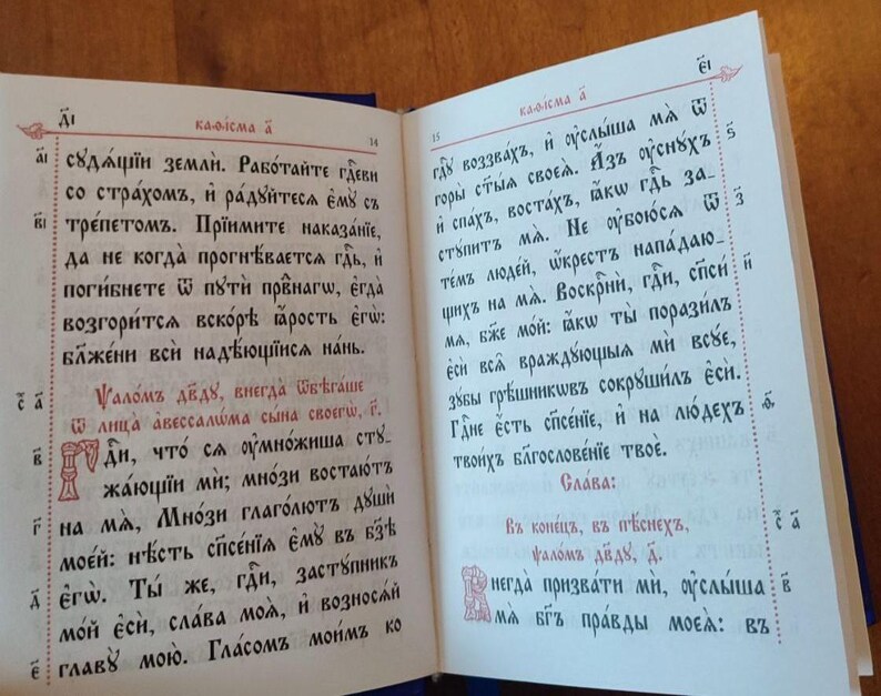 May include: An open book with text in an old Slavic script. The pages are cream-colored with red and black ink. The text is arranged in columns with decorative initial letters.