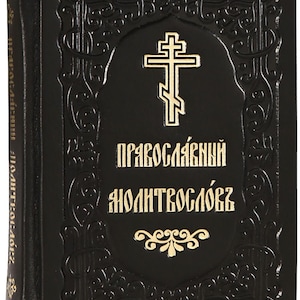 May include: A black book with gold lettering and a gold cross design. The cover features ornate embossed detailing and the title "Православный Молитвословъ". The spine also has text in gold. A religious item.